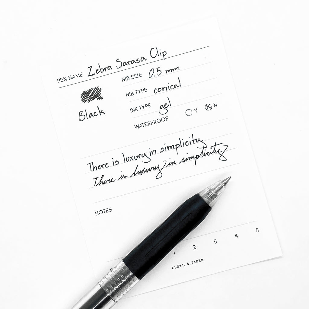 Zebra Sarasa Clip, 0.5 mm, Black, Cloth and Paper. Pen resting on pen test sheet displaying writing sample.