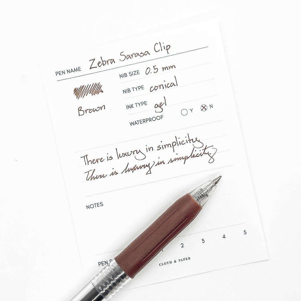 Zebra Sarasa Clip, 0.5 mm, Brown, Cloth and Paper. Pen resting on pen test sheet displaying writing sample.