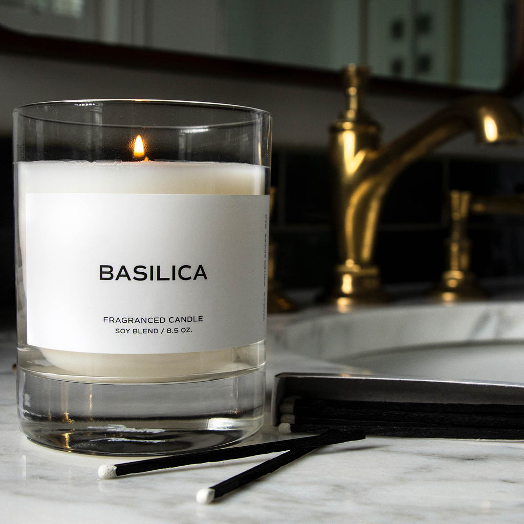 Candle resting on a white marble surface next to matchsticks and a match box. Label on the candle reads "Basilica."
