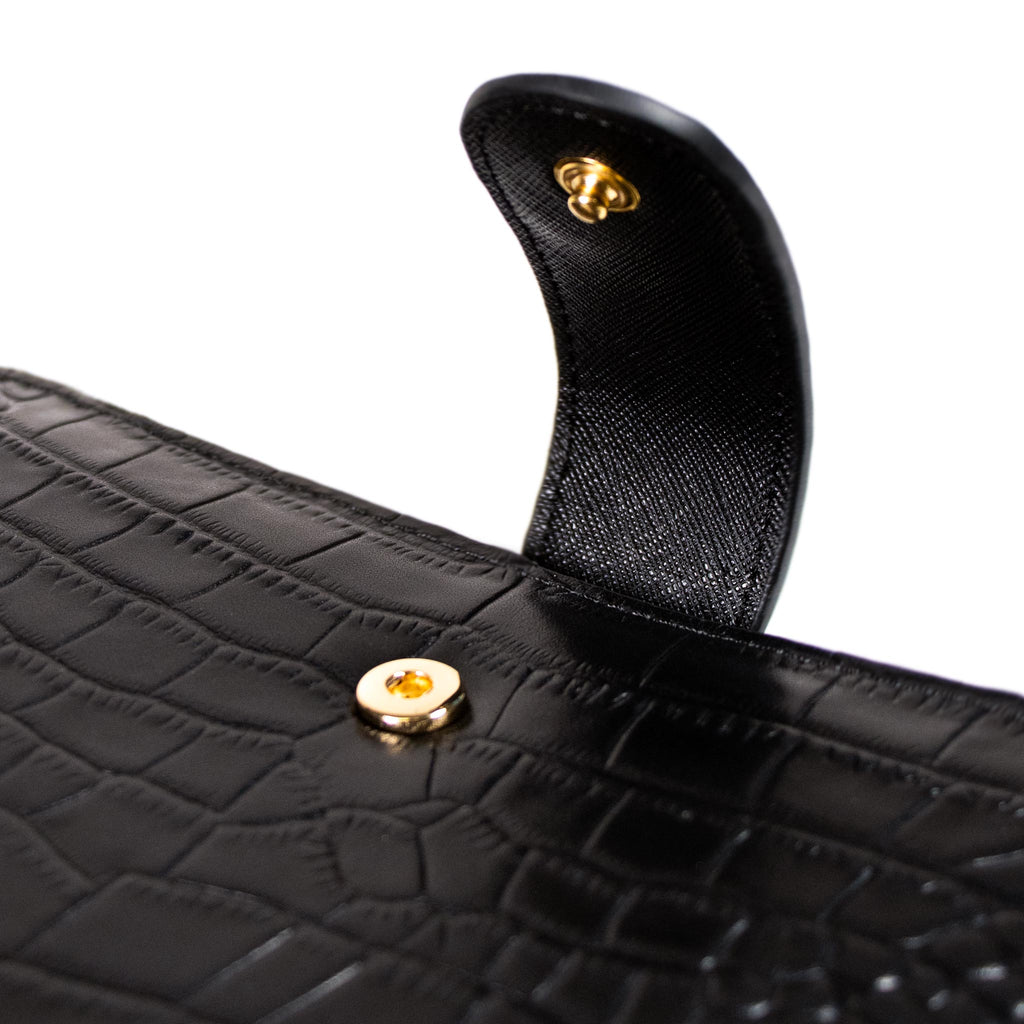 Close up on the snap closure detail of a black croc leather agenda cover with gold snap hardware.