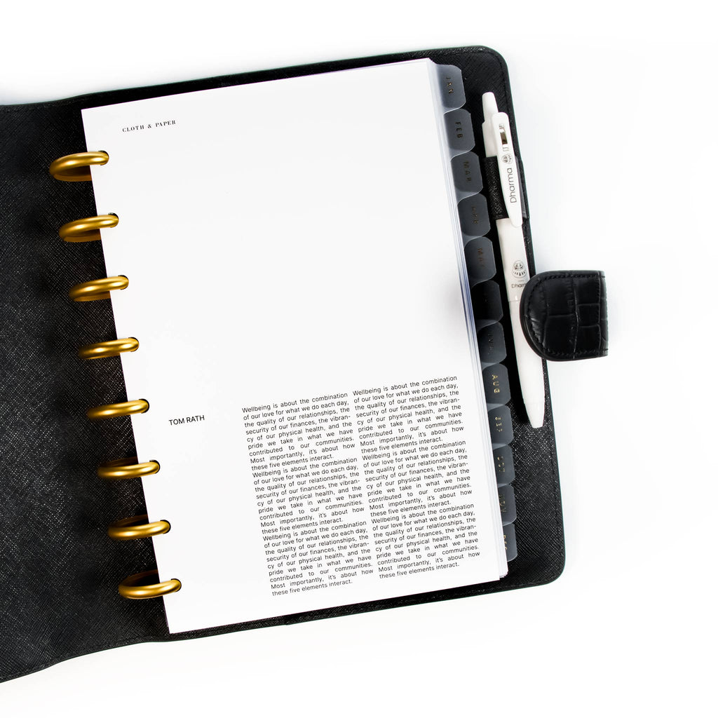 Crosshatch Planner Dashboard styled inside a discbound notebook in a black leather agenda cover. The discbound planner has gold rings, and there is a white pen in the leather cover's pen loop.
