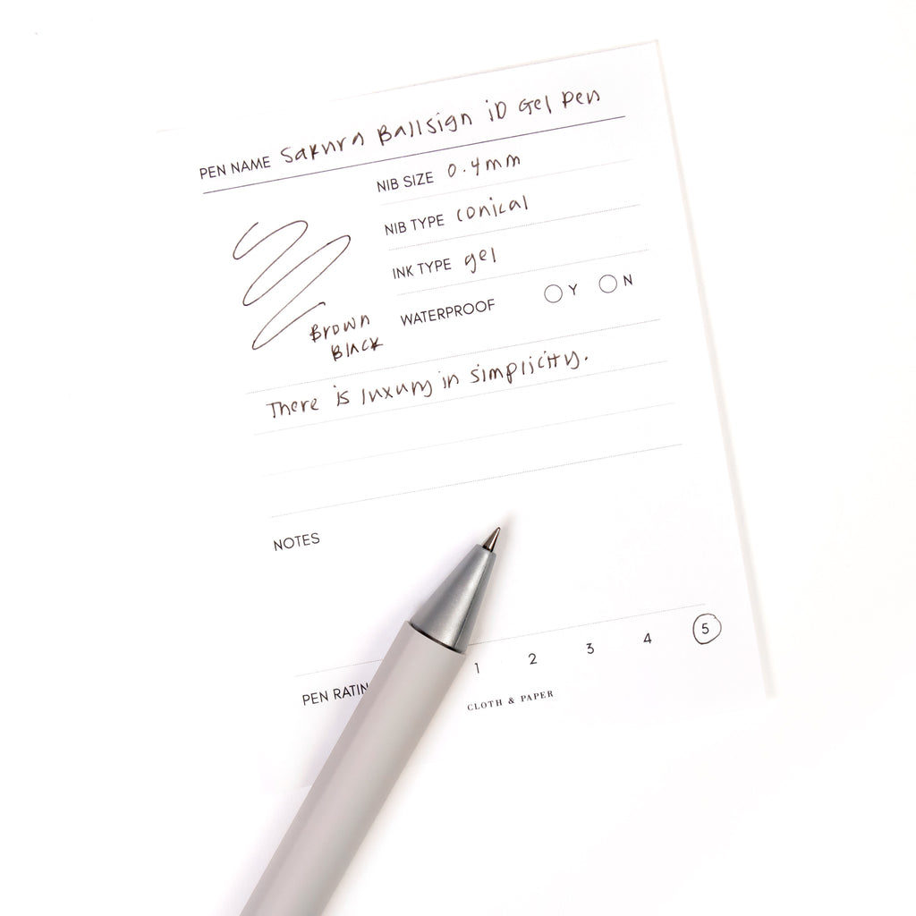 Sakura Ballsign iD Gel Pen, 0.4 mm, Cloth and Paper. Brown black pen resting on pen test sheet displaying writing sample.