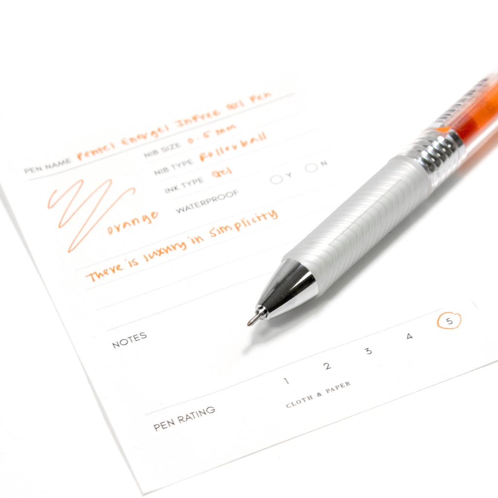 Pentel Energel Infree Gel Pen, Orange, Cloth and Paper. Pen resting on pen test sheet displaying writing sample.