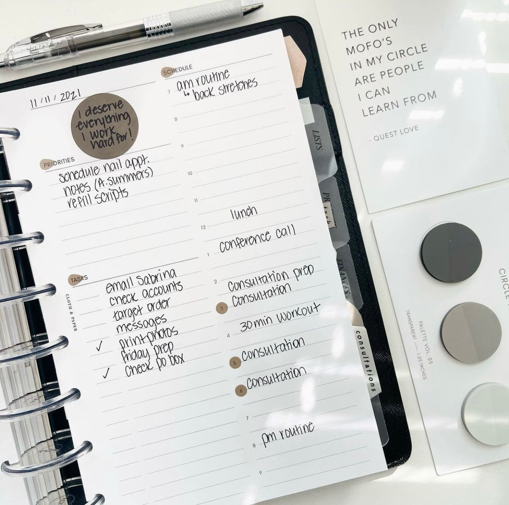 A discbound planner in a cover opened to reveal an Undated Daily Insert filled out with priorities, tasks, and a schedule. Transparent stickers and circle page flags are used on the insert. Next to the planner is a quote card, a pen, and a Circle Page Flag Set.