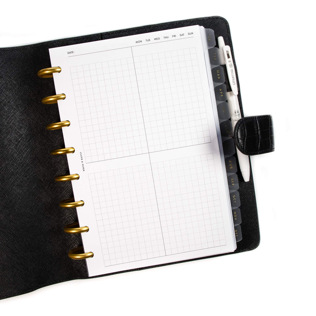 Quad Graph Planner Inserts styled inside a discbound planner tucked into a black leather cover. There is a white pen in the cover's pen loop.