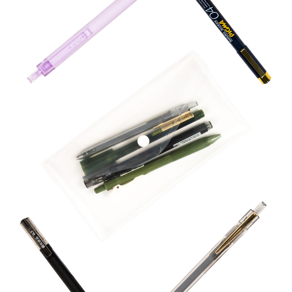 Pens inside pen pouch visible through the transparent material. Pouch is turned to the left against a white background. Other randomly selected pens surround pen pouch, placed at various angles against white background.
