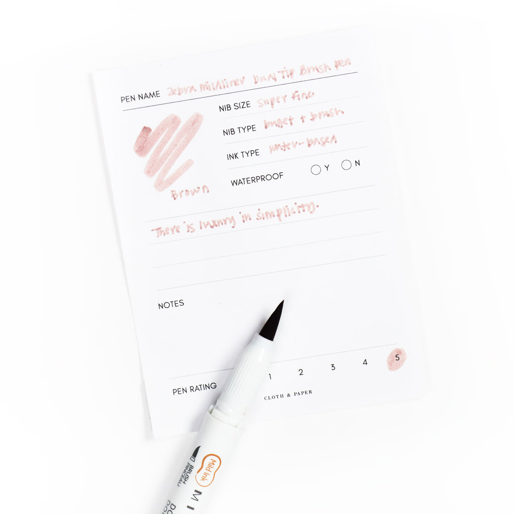 Brush pen tip resting on Brown pen test sheet displaying writing sample that details pen specs.