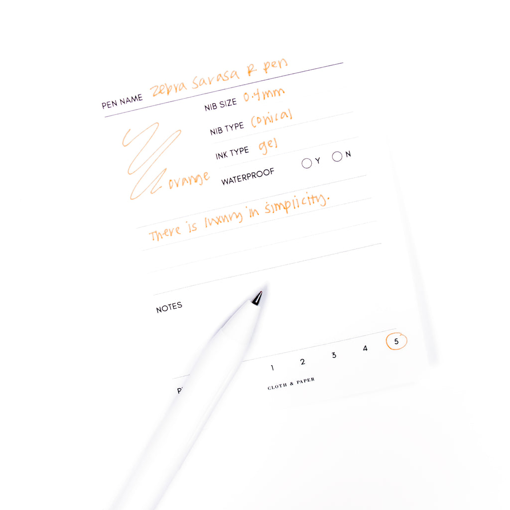 Zebra Sarasa R Pen, 0.4 mm, Orange, Cloth and Paper. Pen resting on pen test sheet displaying writing sample.