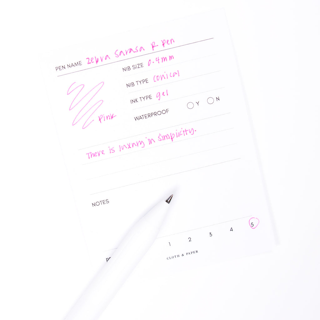 Zebra Sarasa R Pen, 0.4 mm, Pink, Cloth and Paper. Pen resting on pen test sheet displaying writing sample.